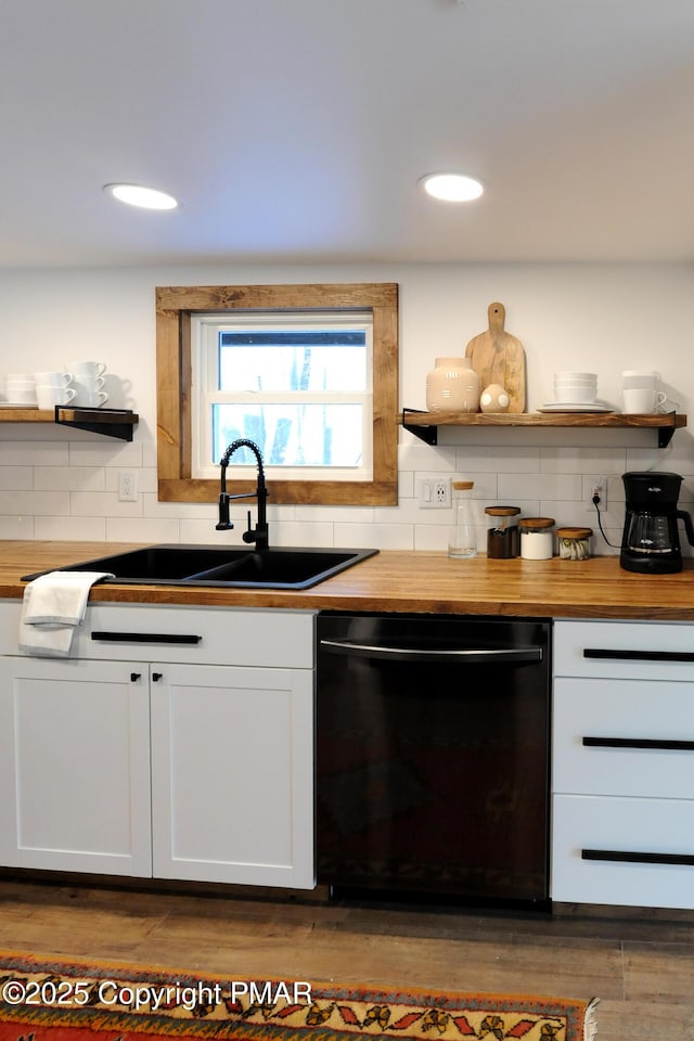 kitchen featuring tasteful backsplash, black dishwasher, sink, wooden counters, and white cabinets