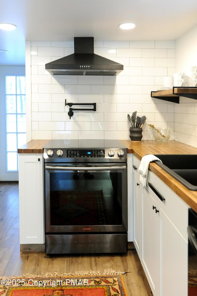 kitchen with white cabinetry, wood counters, island range hood, and stainless steel electric range