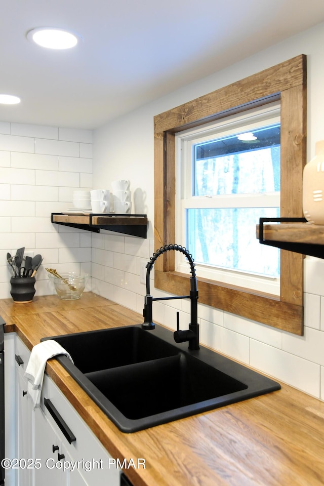 kitchen with sink, butcher block countertops, tasteful backsplash, wood-type flooring, and white cabinets