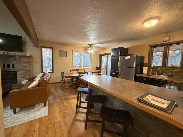 248 Penn Forest Trl, Albrightsville, PA 18210 - kitchen featuring a breakfast bar area, light wood-style flooring, freestanding refrigerator, a brick fireplace, and a sink