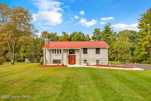 split foyer home with metal roof, fence, stone siding, a chimney, and a front yard