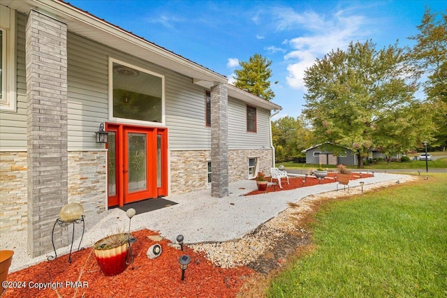 view of exterior entry featuring stone siding and a lawn