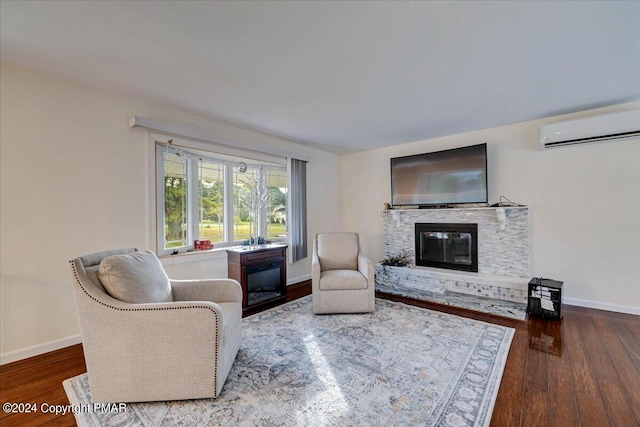 living room featuring a stone fireplace, a wall unit AC, wood finished floors, and baseboards