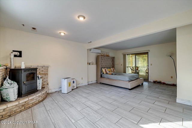 bedroom featuring visible vents, baseboards, a wall mounted air conditioner, a wood stove, and access to outside