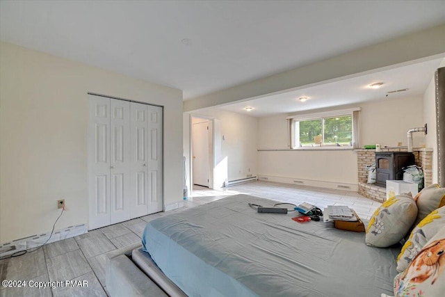 bedroom featuring a closet, a baseboard radiator, a wood stove, and baseboards