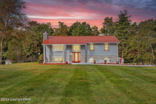 split foyer home with metal roof, stone siding, a front lawn, and a chimney