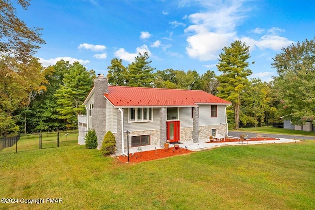 bi-level home with stone siding, fence, metal roof, and a front yard