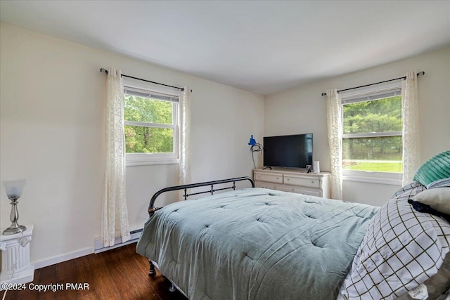 bedroom with baseboards, multiple windows, a baseboard heating unit, and wood finished floors