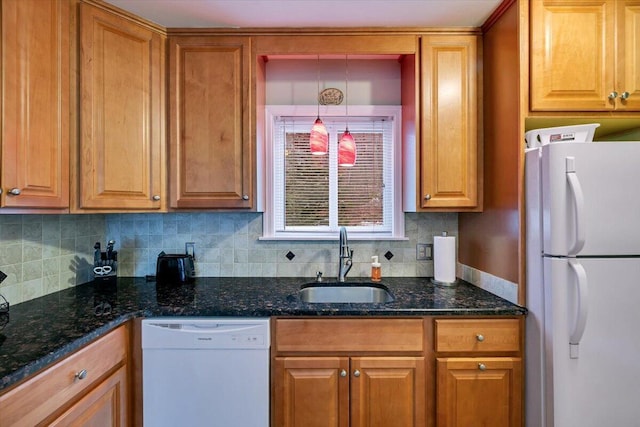 kitchen with white appliances, tasteful backsplash, brown cabinets, dark stone countertops, and a sink