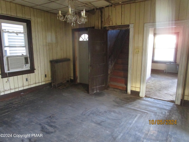 interior space with a notable chandelier, wood walls, cooling unit, and radiator heating unit