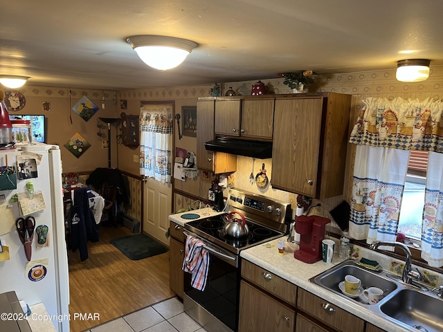 kitchen with electric stove, freestanding refrigerator, light countertops, under cabinet range hood, and a sink