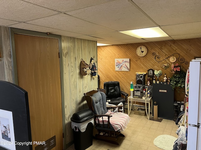 living area with a paneled ceiling, wooden walls, and tile patterned floors