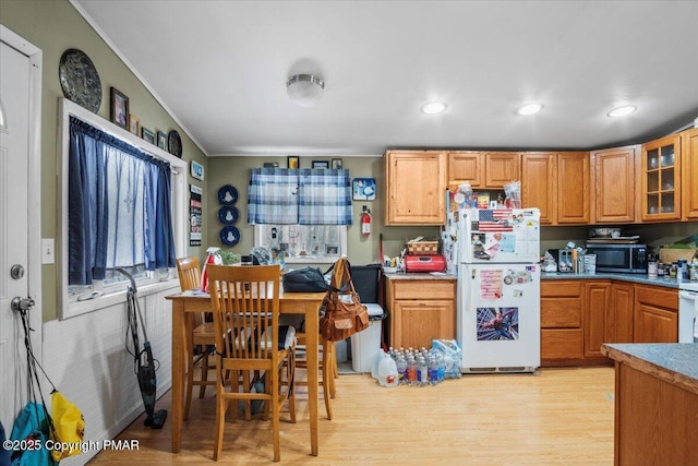 kitchen with light wood-style flooring, freestanding refrigerator, stainless steel microwave, glass insert cabinets, and crown molding