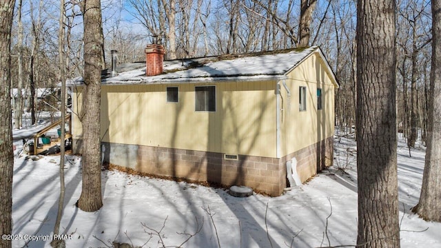 snow covered property featuring a garage, crawl space, and a chimney