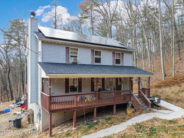 view of front of house with covered porch, a shingled roof, a chimney, and roof mounted solar panels