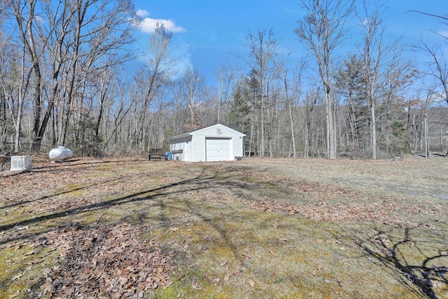 view of yard featuring driveway, a view of trees, a detached garage, and an outdoor structure