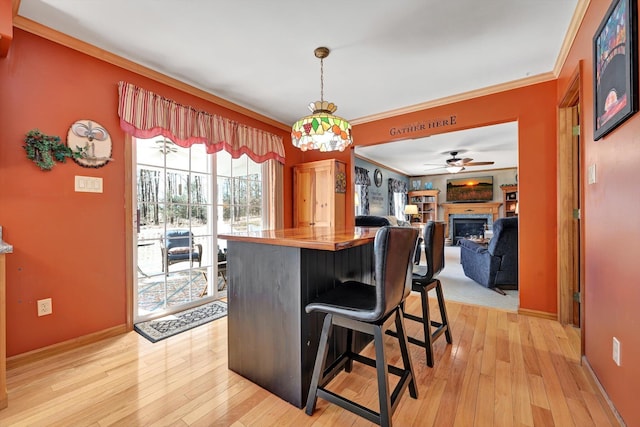 kitchen with baseboards, light wood-style floors, a glass covered fireplace, crown molding, and a kitchen breakfast bar