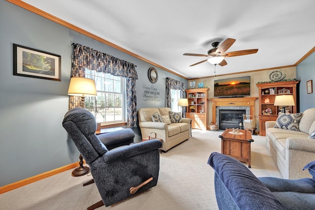 living room featuring a ceiling fan, baseboards, carpet floors, ornamental molding, and a glass covered fireplace