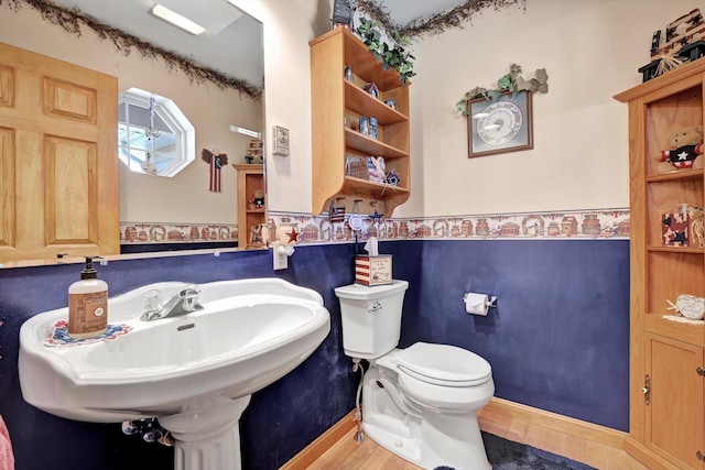 half bath with a wainscoted wall, toilet, and a sink