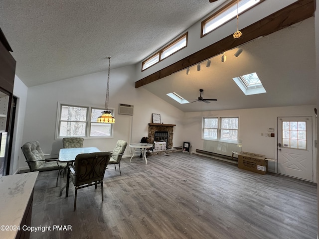 dining room featuring dark wood finished floors, baseboard heating, a textured ceiling, a stone fireplace, and track lighting