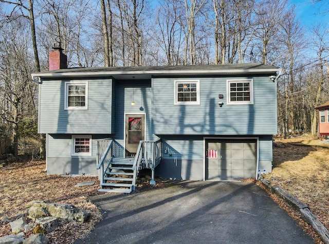 raised ranch with driveway, a chimney, and an attached garage