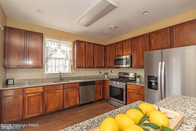 kitchen featuring sink, dark wood-type flooring, backsplash, stainless steel appliances, and light stone counters