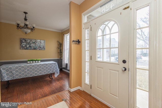 foyer entrance featuring an inviting chandelier, crown molding, a healthy amount of sunlight, and hardwood / wood-style flooring