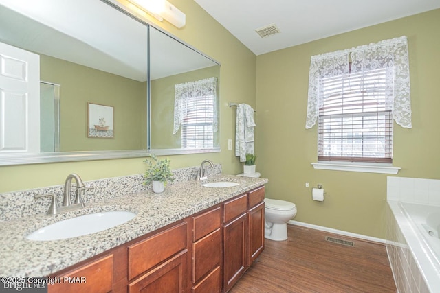 bathroom with hardwood / wood-style flooring, tiled tub, toilet, and a wealth of natural light