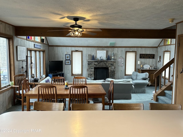 carpeted dining space featuring a stone fireplace, vaulted ceiling with beams, a textured ceiling, and stairs