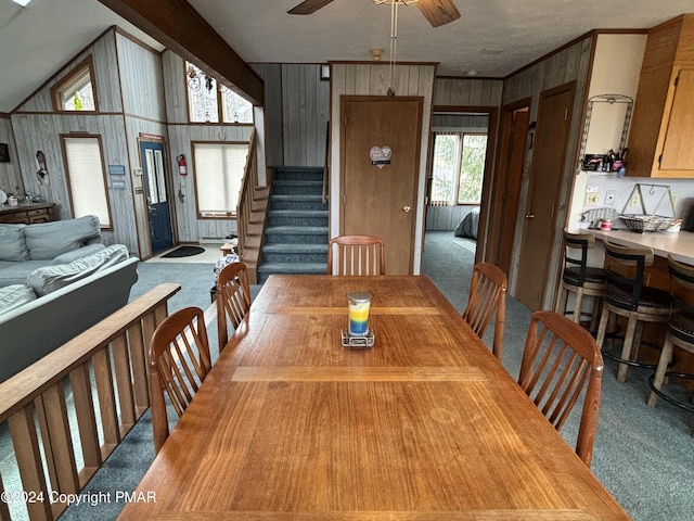 carpeted dining space with ceiling fan, stairway, vaulted ceiling, crown molding, and wood walls