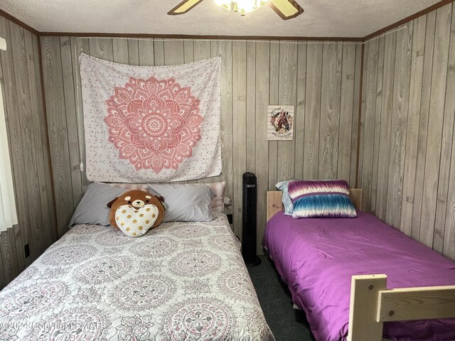 carpeted bedroom featuring ornamental molding, wood walls, a textured ceiling, and ceiling fan