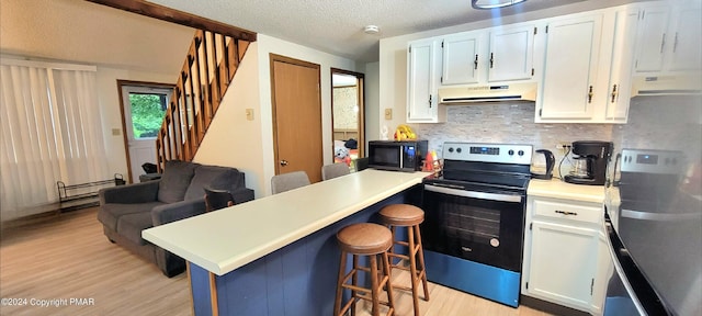 kitchen with black microwave, under cabinet range hood, a breakfast bar, stainless steel range with electric cooktop, and a peninsula