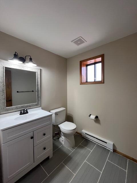 half bathroom featuring visible vents, baseboards, toilet, baseboard heating, and vanity