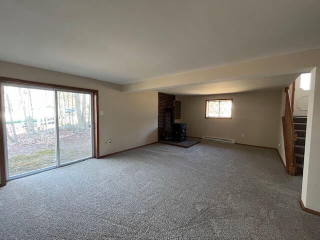 unfurnished living room featuring baseboards, stairs, carpet flooring, a wood stove, and a baseboard radiator