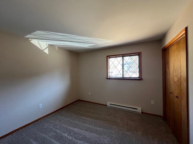 unfurnished bedroom with a closet, baseboards, baseboard heating, and carpet floors