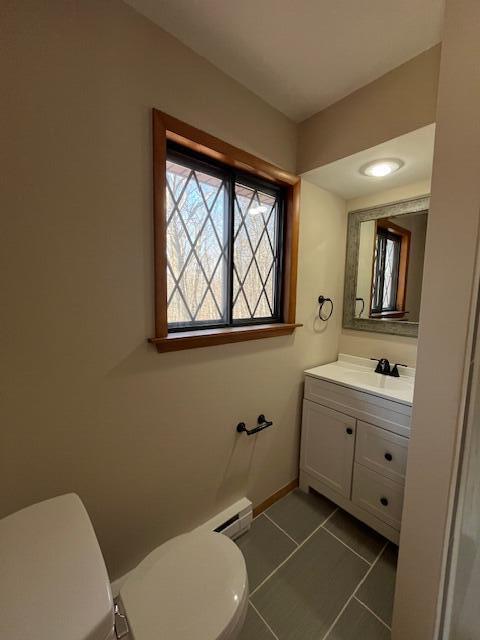 half bath with baseboards, toilet, vanity, and tile patterned flooring