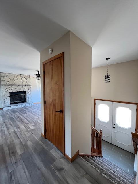 foyer with wood finished floors, french doors, a stone fireplace, baseboards, and ceiling fan