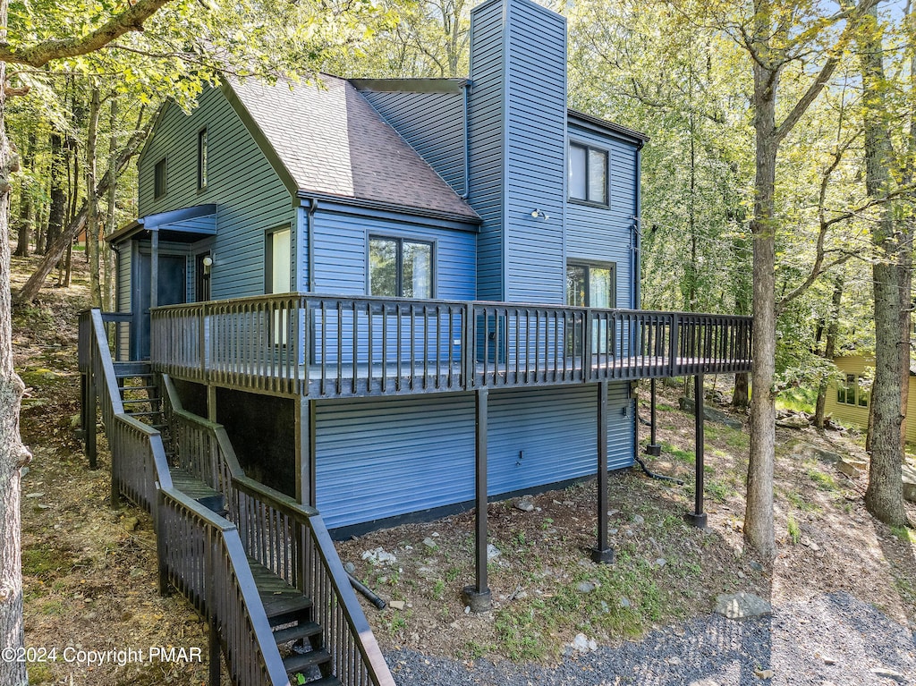 back of property with a deck, a shingled roof, stairway, and a chimney