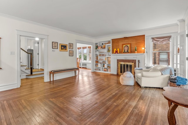 living area featuring baseboards, ornamental molding, a brick fireplace, and stairs