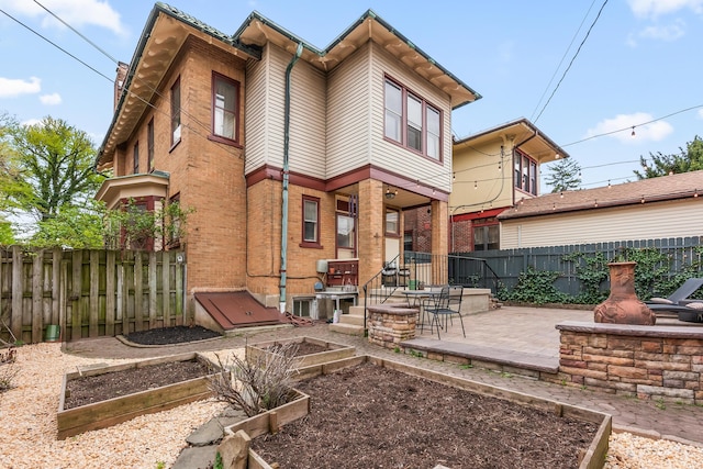 back of house featuring a fenced backyard, a garden, a patio area, and brick siding