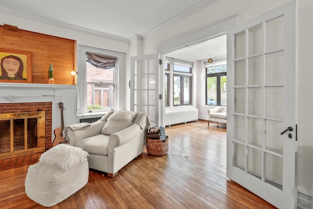 sitting room featuring wood-type flooring, ornamental molding, radiator heating unit, and a fireplace