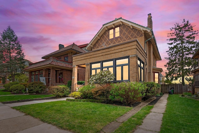 view of front of home featuring brick siding, a front lawn, fence, and a chimney