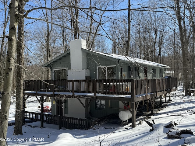 snow covered back of property with a chimney and a deck