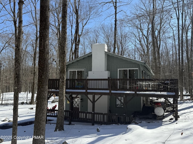 snow covered house featuring a chimney and a wooden deck