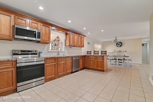 kitchen featuring a peninsula, brown cabinetry, stainless steel appliances, and a sink