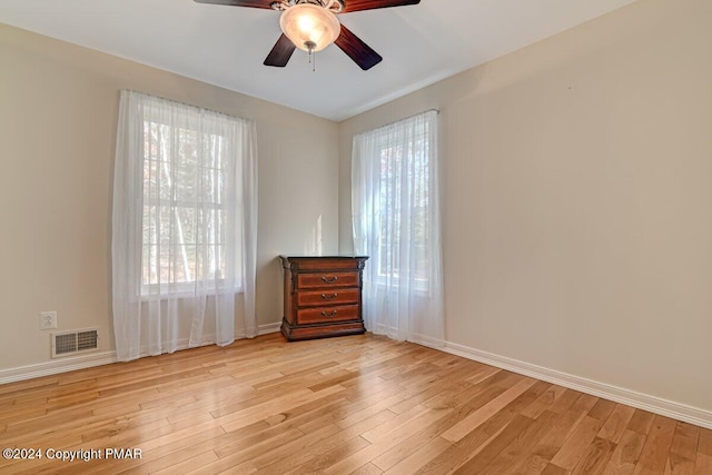 unfurnished room with a ceiling fan, light wood-type flooring, visible vents, and baseboards