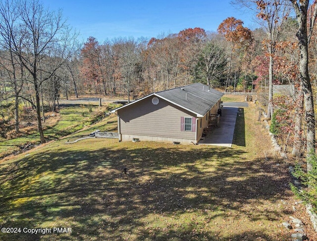 view of side of home with crawl space, a forest view, and a lawn