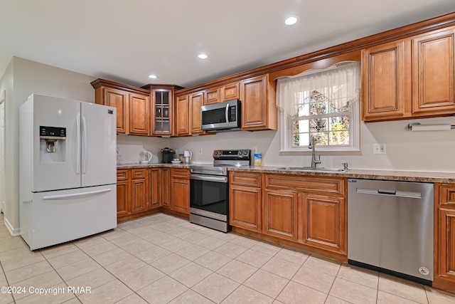 kitchen with glass insert cabinets, appliances with stainless steel finishes, brown cabinets, a sink, and recessed lighting