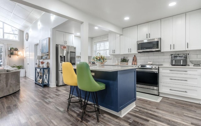 352 Scotch Pine Dr, Pocono Summit, PA 18346 - kitchen with appliances with stainless steel finishes, dark wood-style floors, decorative backsplash, a center island, and light countertops