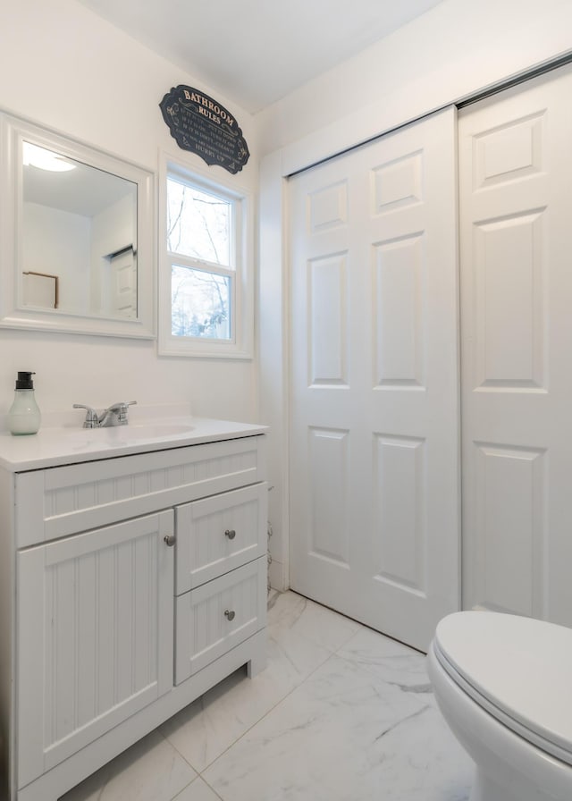 half bathroom featuring toilet, marble finish floor, and vanity